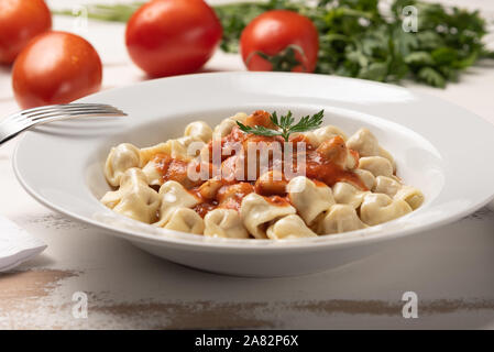 Italienisch Tortellini (capeletti, Agnolini) mit Tomatensauce in eine weiße Platte auf rustikalen Holztisch Hintergrund weiss Stockfoto