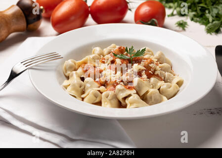 Italienisch Tortellini (capeletti, Agnolini) mit Tomatensauce in eine weiße Platte auf rustikalen Holztisch Hintergrund weiss Stockfoto