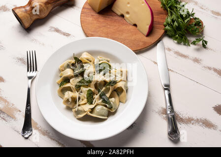 Hausgemachte Tortellini mit Butter und Salbei in einer weißen Platte auf weiße Holztisch Hintergrund. Weiches Licht Stockfoto