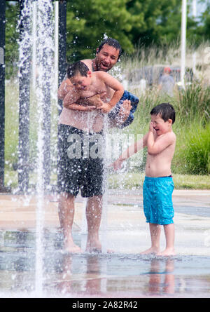 Ein Papa spielt mit seinem Lachen Söhne, in einem nassen Splash pad Brunnen Stockfoto