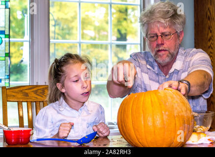 Ein kleines Mädchen beobachtet, wie Opa macht empfindliche Einschnitte in den Betrieb von Carving ein jack o lantern Stockfoto