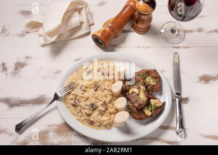 Risotto mit Filet Mignon. Risoto und Rindfleisch mit Kapern und Pilze in einer weißen Platte auf einem weißen Hintergrund. Italienisches Essen. Stockfoto