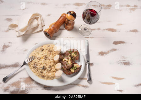Risotto mit Filet Mignon. Risoto und Rindfleisch mit Kapern und Pilze in einer weißen Platte auf einem weißen Hintergrund. Italienisches Essen. Stockfoto