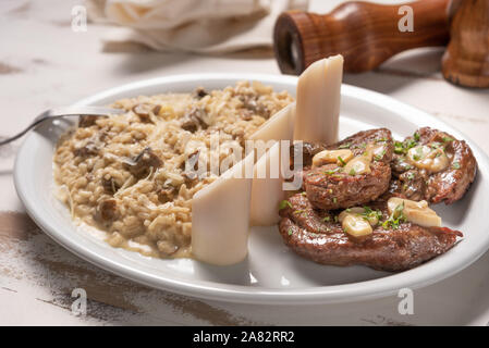 Risotto mit Filet Mignon. Risoto und Rindfleisch mit Kapern und Pilze in einer weißen Platte auf einem weißen Hintergrund. Italienisches Essen. Stockfoto