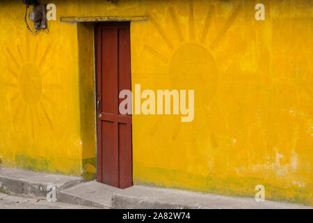 Ein hell gestrichenen Wand- und rote Tür eines Hauses in San Pedro La Laguna, Guatemala. Eine Darstellung der Sonne ist in der Malerei. Stockfoto