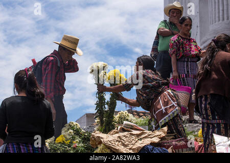 Eine Quiche Maya Frau in traditioneller Kleidung Verkauf von einem Mann Blumen auf den Stufen der Kirche von Santo Tomas in Chichicastenango, Guatemala. Stockfoto