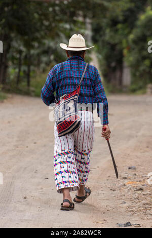 Eine ältere Maya Bauer das Tragen der Tracht von San Pedro La Laguna, Guatemala, zu seinem kleinen Bauernhof auf einer Schotterstraße, Durchführung einer Machete Stockfoto