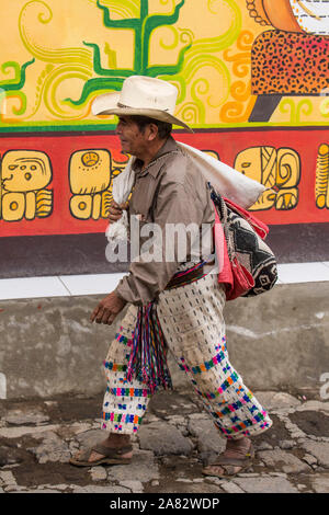 Ein Maya Bauer in traditioneller Kleidung Spaziergänge entlang einer Straße vor einer bemalten Wand in San Pedro La Laguna am Lago Atitlan in Guatemala. Stockfoto