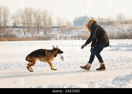 Stilvolle Kerl Spaziergang mit dem Hund. Spaß im Schnee spielen im Freien. Spielerische. Tierliebhaber. Deutscher Schäferhund genießen Sie die Freiheit. Freunde zusammen. Lustige e Stockfoto