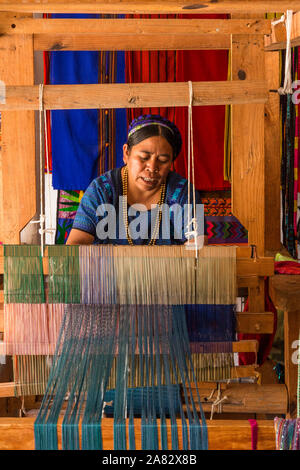 Eine Maya-Frau, trägt typische Tracht webt Stoff auf einem Fuß betätigt Webstuhl in Werkstatt in San Antonio Palopó, Guatemala. Stockfoto