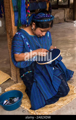 Eine junge Frau Maya im typischen Kleid hand-Stickt Panels von Handgewobenen Stoff zusammen eine traditionelle huipil oder Bluse zu machen. Stockfoto