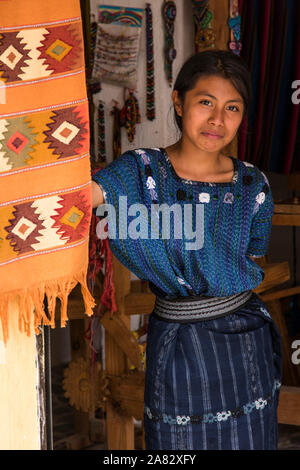 Eine attraktive junge Frau Maya tragen typische Kleid sieht vor die Tür einer Familie Weberei in San Antonio Palopó, Guatemala. Stockfoto