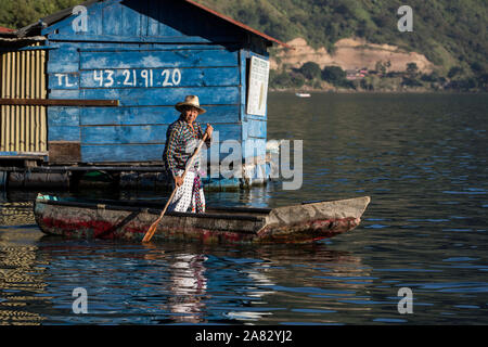 Maya Mann in die traditionelle Kleidung der San Pedro La Laguna steht wie er Paddel seine cayuco am frühen Morgen Licht auf - Atitlan See, Guatemala. Stockfoto
