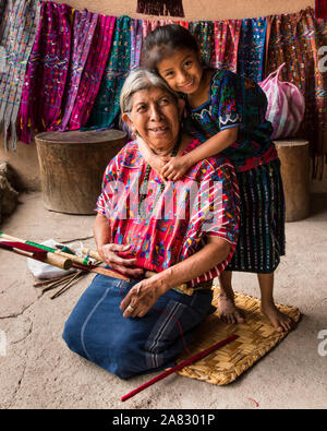 Eine junge GUATEMALTEKISCHE Maya Mädchen in traditioneller Kleidung, umarmt sie Großmutter, kniet und Weberei auf einem backstrap Webstuhl. Santa Catarina Palopo, Gu Stockfoto