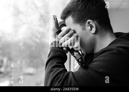 Schwarz-weiß Foto junger Mann mit Gewehr, Selbstmord zu begehen, in der Nähe der Fenster Stockfoto