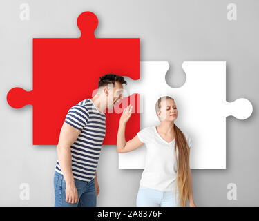 Junge Paare streiten und Teile Puzzle auf hellen Hintergrund Stockfoto
