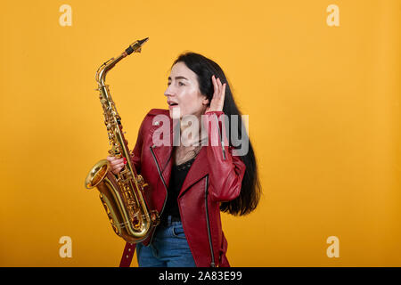 Junge traurig besorgt Frau in rad Jacke suche Kamera, gold Saxophon Stockfoto