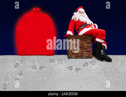 Santa Claus sitzt auf dem Schornstein an einem verschneiten Dach mit einer großen Tüte voller Weihnachtsgeschenke, Hintergrund von dunklem Blau mit Sternen. Stockfoto