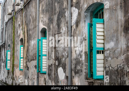 Eine Linie der offenen Fenster mit grünen Fensterläden aus Holz an der Fassade eines alten Hauses. Stockfoto