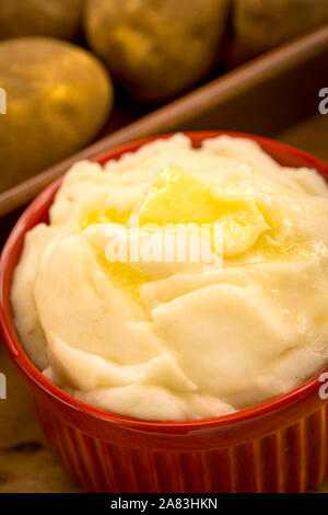 Kartoffelpüree in rotem Ramekin mit Butter mit Kartoffeln im Hintergrund Stockfoto