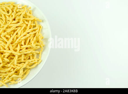 Italienische traditionelle hausgemachte Pasta. Ungekochte Pasta Strozzapreti in einem weißen Teller auf weißem Hintergrund. Direkt darüber. Stockfoto