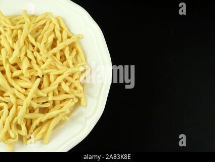 Italienische traditionelle hausgemachte Pasta. Ungekochte Pasta Strozzapreti in einem weißen Teller auf dunklem Hintergrund. Direkt darüber. Stockfoto