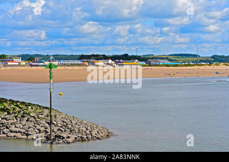 Eine Ansicht von Sandy Bay Porthcawl im Sommer. Menschen am Sandstrand mit Kirmes & Arkaden hinter sich. Wellenbrecher am Eingang der Marina. Stockfoto