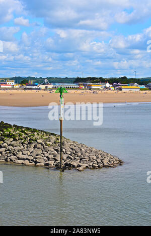 Eine Ansicht von Sandy Bay Porthcawl im Sommer. Menschen am Sandstrand mit Kirmes & Arkaden hinter sich. Wellenbrecher am Eingang der Marina. Stockfoto