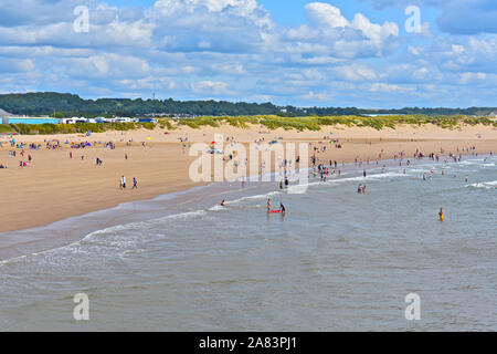 Einen Panoramablick über zu Sandy Bay Beach in Porthcawl im Sommer. Die Menschen genießen, Spielen, plantschen und schwimmen im Meer. Kirmes hinter sich. Stockfoto
