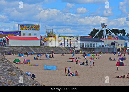 Ein Blick auf Sandy Bay Beach in Porthcawl im Sommer. Leute genießen spielen, paddeln und Schwimmen im Meer. Coney Strand Kirmes hinter sich. Stockfoto