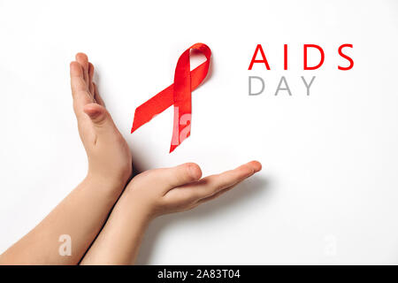 Nahaufnahme Bild horizontal der Hände des Kindes holding red ribbon auf weißem Hintergrund, HIV Bewußtsein Konzept, Welt-AIDS-Tag. Flach, Ansicht von oben, kopieren Spa Stockfoto