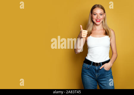 Glückliche junge Frau Daumen oben auf gelben Hintergrund. Positive emotion Stockfoto