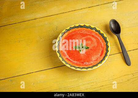 Gazpacho Suppe mit grünem Basilikum in gelb Schüssel auf rustikalen Hintergrund. Traditionelle spanische kalte Suppe pürieren. Stockfoto