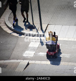 Behinderte Menschen mit elektrischen Rollstuhl gehen durch einen Zebrastreifen in einer Straße. Stockfoto