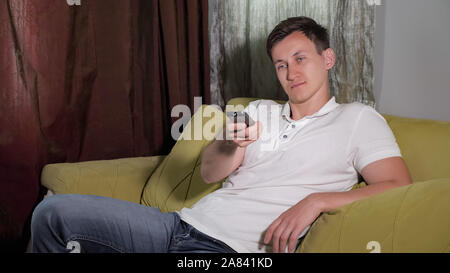 Junge lachen Mann im weißen T-Shirt ist auf dem Sofa sitzen vor dem Fernseher, close-up Stockfoto