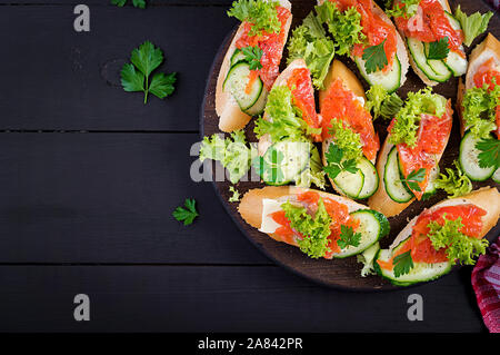 Tapas. Gesalzenen Lachs, Butter und Gurken toast Sandwiches auf Holzbrett. Ansicht von oben Stockfoto