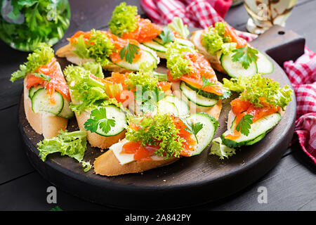 Tapas. Gesalzenen Lachs, Butter und Gurken toast Sandwiches auf Holzbrett. Stockfoto