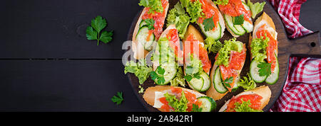 Tapas. Gesalzenen Lachs, Butter und Gurken toast Sandwiches auf Holzbrett. Banner. Ansicht von oben Stockfoto