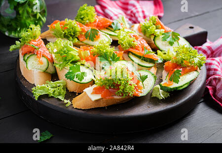 Tapas. Gesalzenen Lachs, Butter und Gurken toast Sandwiches auf Holzbrett. Stockfoto