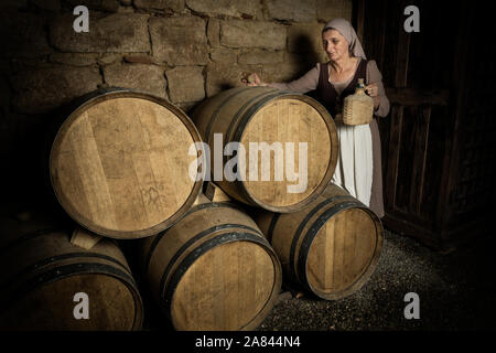 Die Frau in der mittelalterlichen bäuerlichen Outfit prüfen Wein Fässer im Keller einer Eigenschaft freigegeben Authentische mittelalterliche Schloss in Frankreich Stockfoto