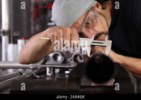 Hände mann Nahaufnahme Arbeit in Home Werkstatt garage mit Messschieber messen Metall Rohr in den Schraubstock an der Werkbank, diy und Handwerk Konzept fest Stockfoto