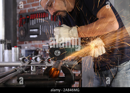 Mann Arbeit in Home Werkstatt garage cut Metall Rohr, Schutzbrille und Handschuhe, Schneiden von Metall macht Funken, Nahaufnahme, Heimwerker- und craft-Konzept Stockfoto