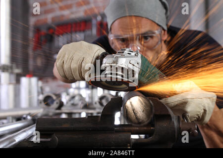 Mann Arbeit in Home Werkstatt garage mit Winkelschleifer, Schutzbrille und Handschuhe, Schleifen von Metall macht Funken, Nahaufnahme, Heimwerker- und craft-Konzept Stockfoto