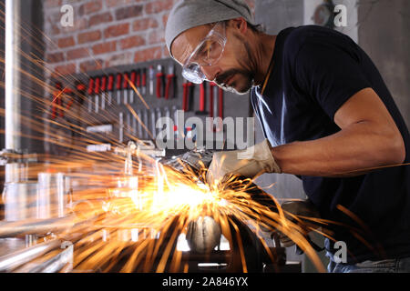 Mann Arbeit in Home Werkstatt garage mit Winkelschleifer, Schutzbrille und Handschuhe, Schleifen von Metall macht Funken, Nahaufnahme, Heimwerker- und craft-Konzept Stockfoto
