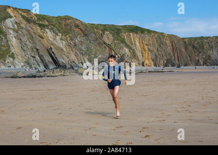 Ein kleiner Junge, der an einem leeren Strand in Großbritannien läuft. Stockfoto