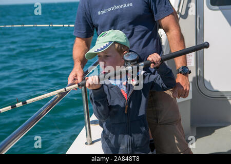 Ein kleiner Junge, der eine Angelrute auf einem Boot auf See, Devon, Großbritannien, hält. Stockfoto