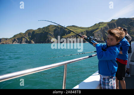 Ein kleiner Junge, der eine Angelrute auf einem Boot auf See, Devon, Großbritannien, hält. Stockfoto