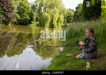 Ein kleiner Junge, der seine Angelrute neben einem See hält. Stockfoto