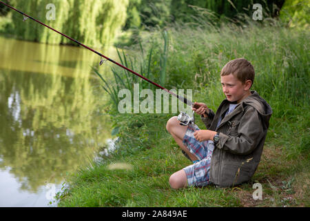 Ein kleiner Junge, der seine Angelrute neben einem See hält. Stockfoto