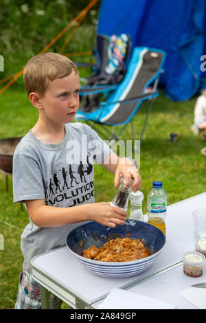 Ein kleiner Junge würzt frischen Tintenfisch, der bereit ist, auf dem BBQ zu gehen, Großbritannien. Stockfoto